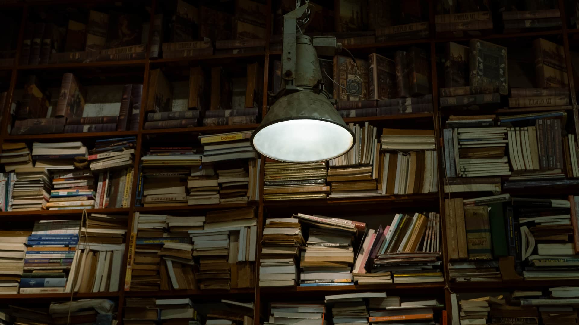 A dimly lit library bookcase under a single warm lamp